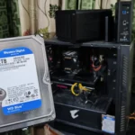 Một người cầm ổ cứng HDD trước máy tính và hai thiết bị NAS TerraMaster, minh họa cho vấn đề thiếu không gian lưu trữ PC và giải pháp từ NAS.