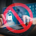 Bàn tay gõ laptop với biểu tượng cấm màu đỏ che các icon bảo mật, ám chỉ hạn chế quyền truy cập kỹ thuật số.