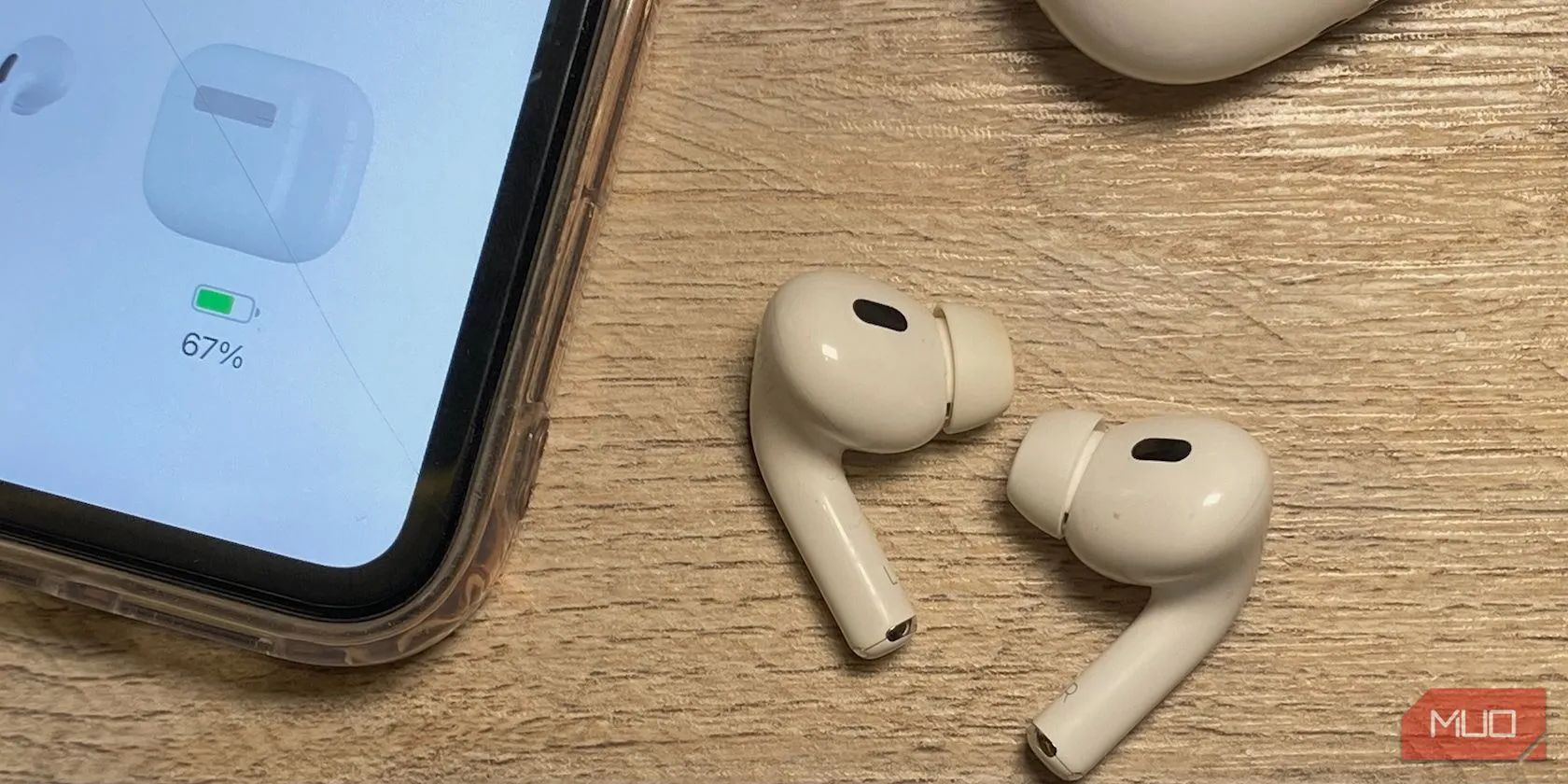Hai cặp tai nghe AirPods màu trắng đặt cạnh iPhone trên bàn gỗ, một cặp có thân ngắn và một cặp thân dài, thể hiện sự khác biệt về chiều dài thân của các thế hệ AirPods