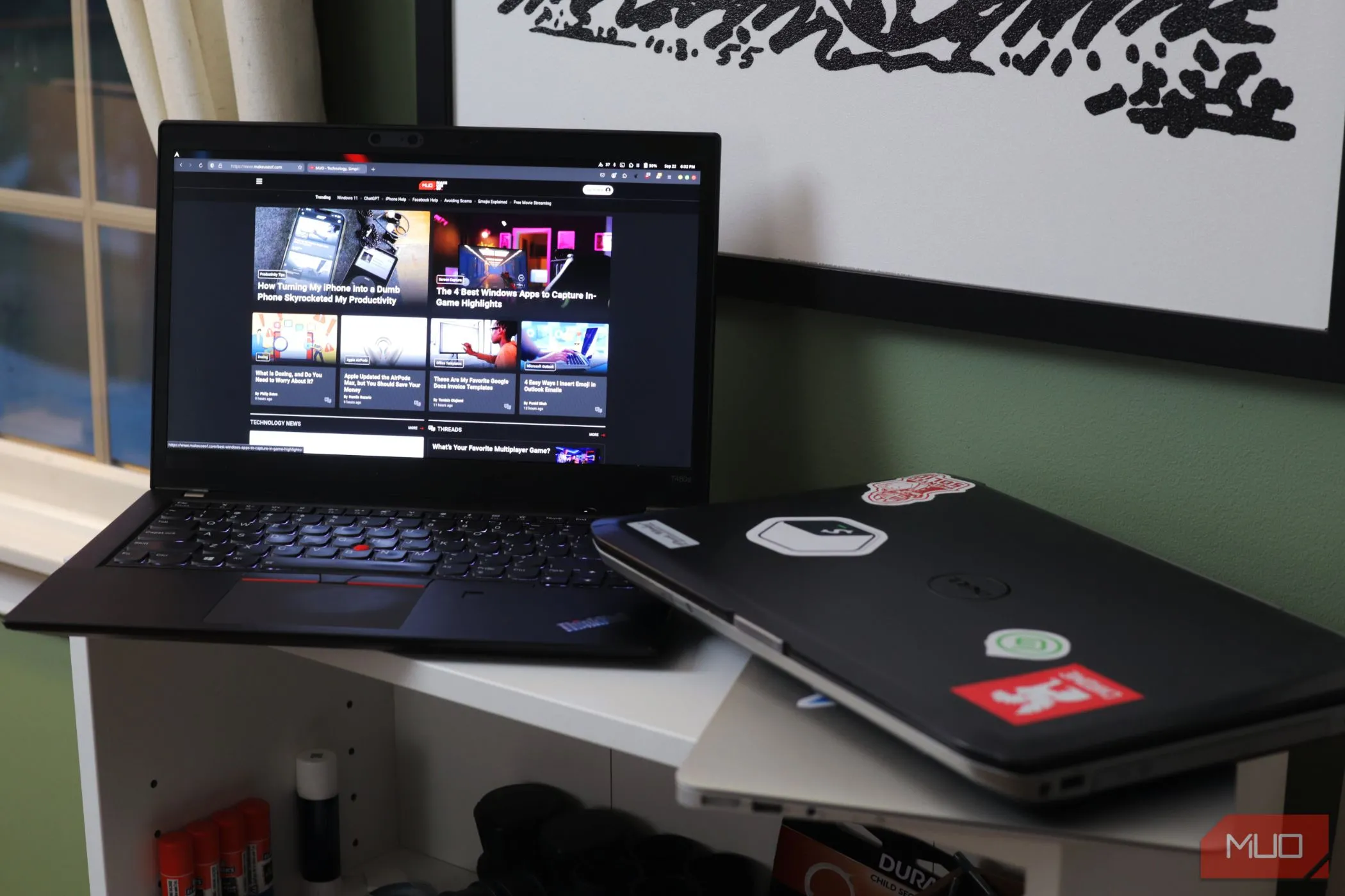 Hai chiếc laptop trên kệ trắng, một chiếc đang mở trang MakeUseOf.