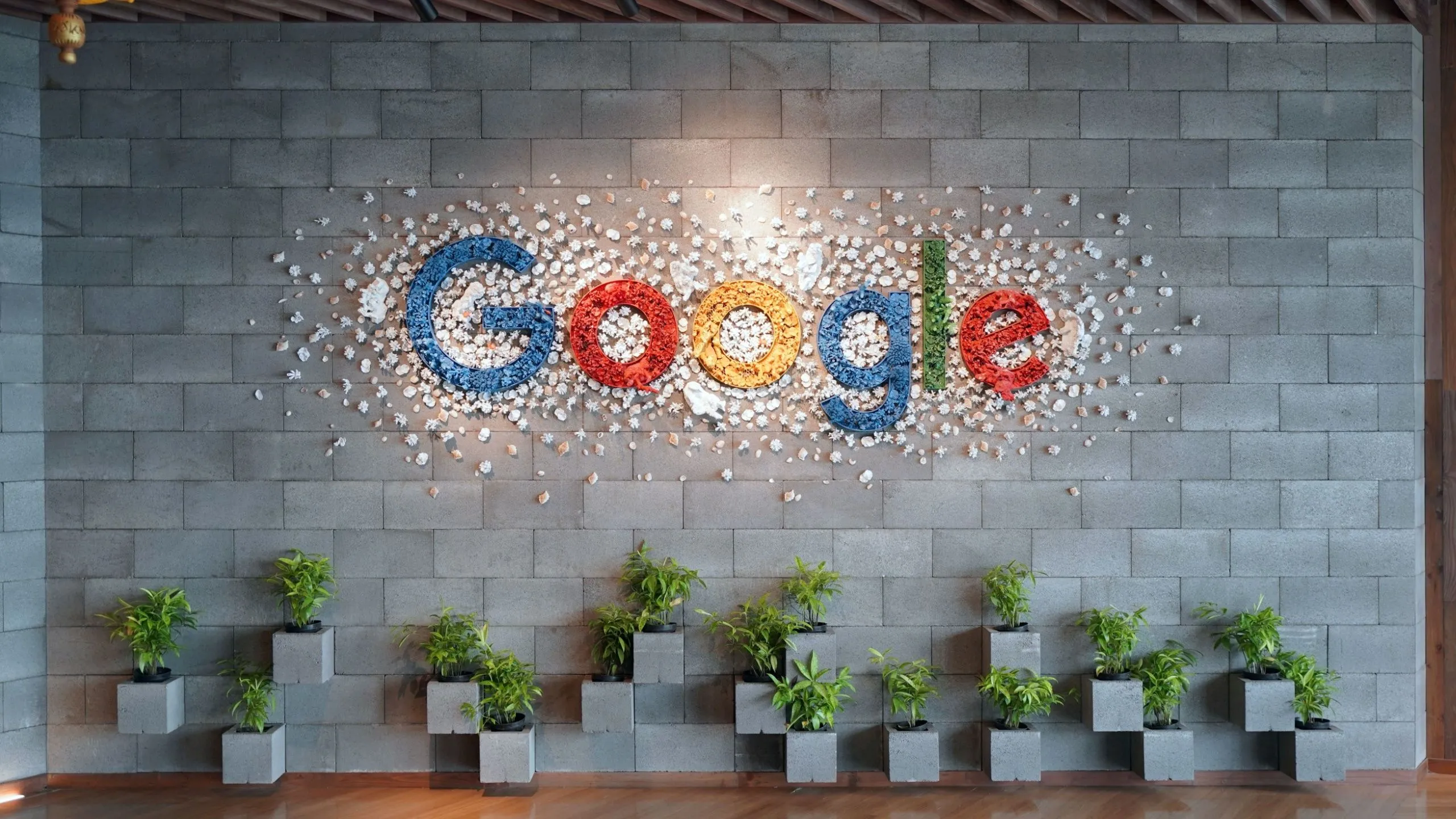Logo Google trên tường văn phòng với cây xanh, thể hiện sự đồng bộ hóa liền mạch của Chromebook với hệ sinh thái Google