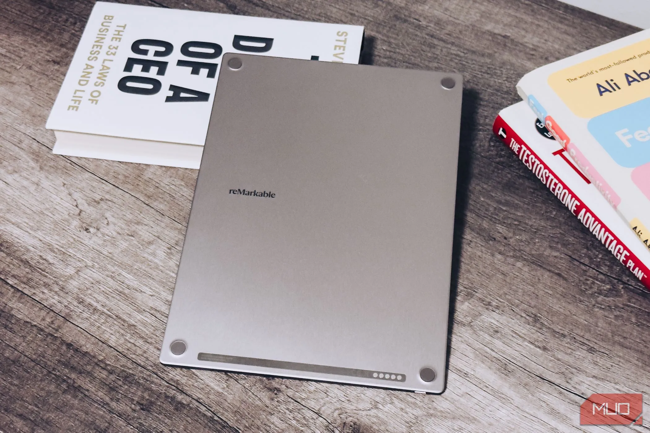 Mặt sau của reMarkable Paper Pro đặt trên bàn gỗ, cạnh một chồng sách, thể hiện thiết kế tổng thể và các miếng đệm cao su