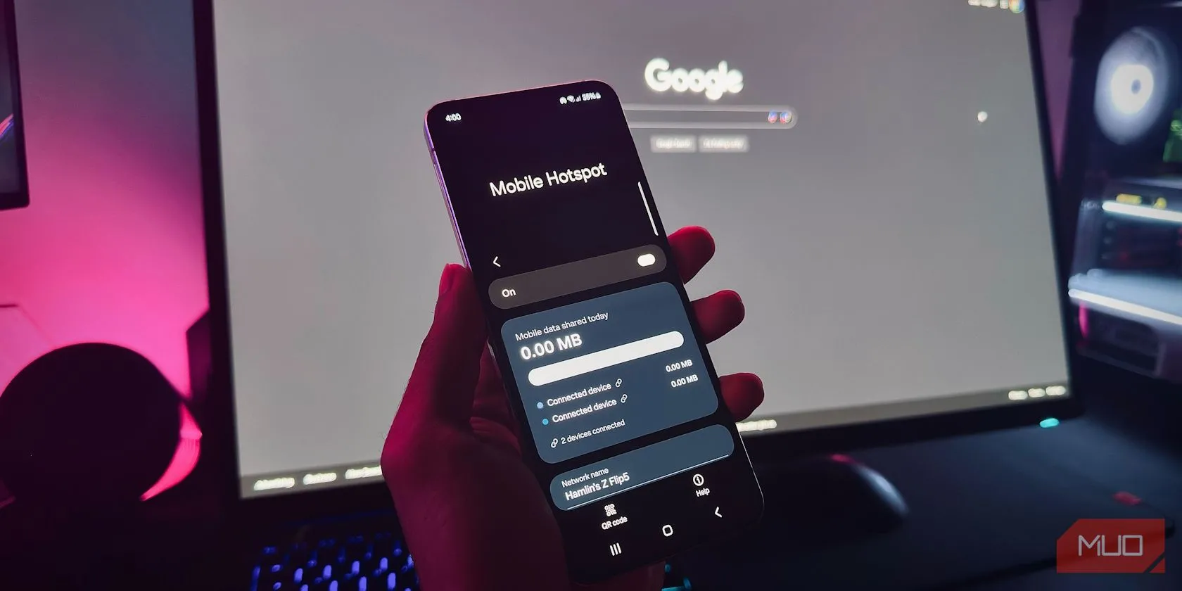 Người dùng đang cầm điện thoại Android hiển thị tính năng Mobile Hotspot trước màn hình máy tính.